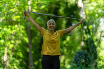 Senior woman exercising with elastic resistance band for strength training in the park.