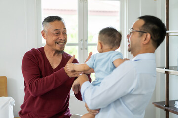 Joyful moment of multigenerational family at home, father holding up his baby smiling and playing while the grandfather looks on with a big smile enjoying the happy interaction, love within a family