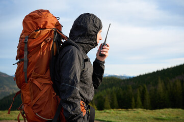 Fully equipped hiker talking by walkie-talkie on the peak of the mountain. Tourist talking by the...