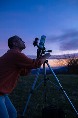 Amateur astronomer looking at the evening skies, observing planets, stars, Moon and other celestial objects with a telescope.