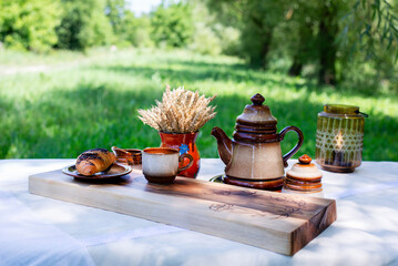 A cup of coffee and a teapot on a tray. Kitchen board. Ears of wheat in a jug.