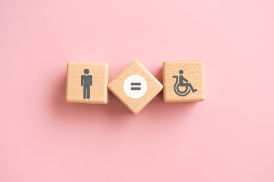 Symbol for equal rights of persons with disabilities. Man , disability person and equal sign on wooden cube blocks with pink background