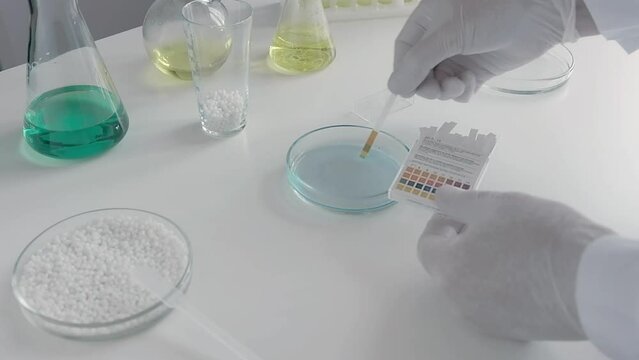 A scientist in a chemical laboratory takes measurements of the acid-base balance of a liquid in a petri dish.