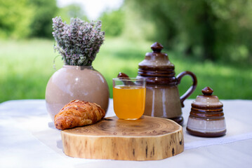 Croissant and a glass of orange juice on a tray. Kitchen board. A bouquet of lavender in a vase.