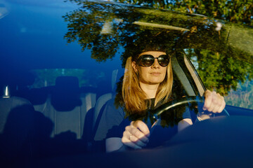 Woman enjoys new car. Happy female driver wearing sunglasses is sitting in car, view through windshield