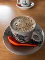 Top view of bubbles on the white coffee served in Kopitiam cup on the wooden table.