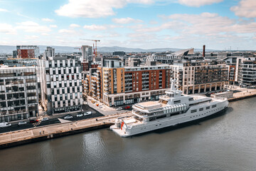 Naklejka premium Modern Waterfront in Dublin Featuring Luxury Yacht, Contemporary Architecture, and Scenic Urban Landscape under Clear Blue Sky
