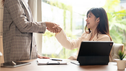 An Asian businesswoman or female office worker is shaking hands with her colleague in the meeting.