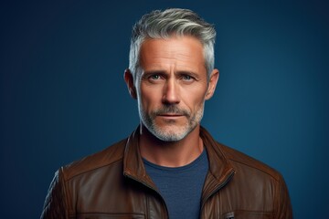 Fototapeta premium A man with a beard and gray hair is wearing a brown jacket and blue shirt