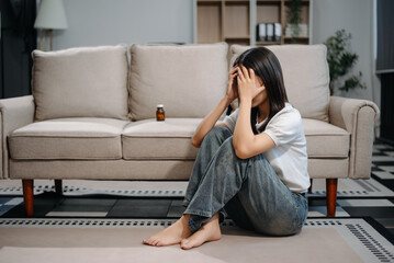 Asian woman sit Depression Dark haired  pensive glance Standing by window and anxiety Copy space with a blanket on a sofa.