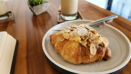 Home made croissants with almond toppings on a white plate served with ice coffee on the woody table at cafe