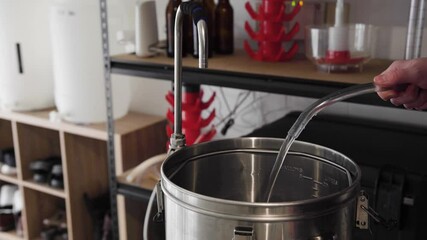 Water pouring into and filling up a metal pot in a home beer brewing setup, close up