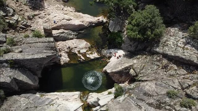 drone shot of person jumping into natural rock pool in sardegna italy