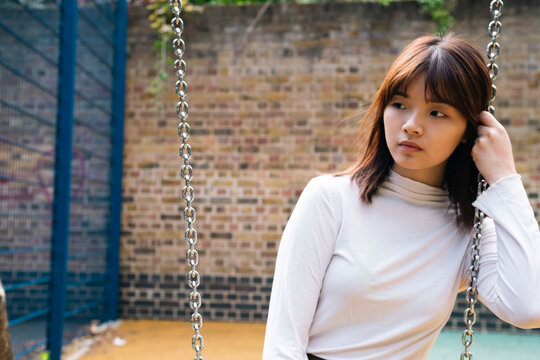 Thoughtful young woman sitting on swing at playground