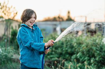 Cheerful boy watering plants in vegetable garden