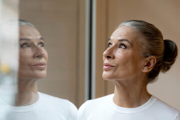 Senior gray haired woman with reflection on window