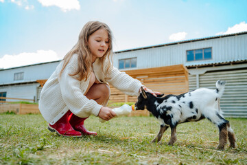 Girl feeding milk to kid goat in farm
