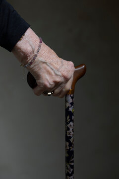 Hand of senior woman holding walking cane against black background