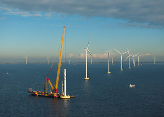 Crane vessel constructing wind turbine in IJsselmeer lake under cloudy sky