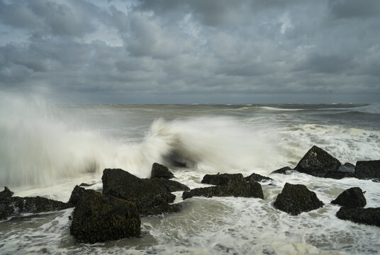 Waves hitting rocks during storm under cloudy sky in North Sea