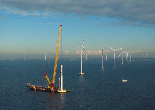 Crane vessel constructing wind turbine in IJsselmeer lake under cloudy sky