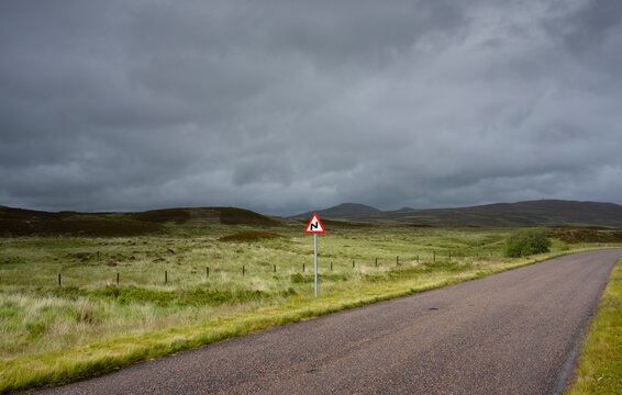 Empty road with warning sign amidst agricultural field in Scottish Highlands