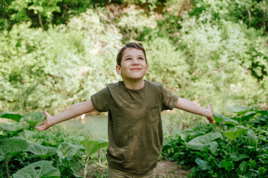 Smiling boy arms outstretched looking up at forest - Powered by Adobe