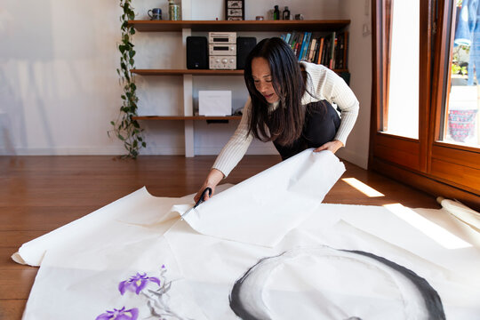Woman painter cutting washi paper with scissors at home