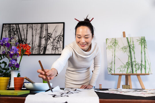Happy woman artist writing in Japanese on white paper at home