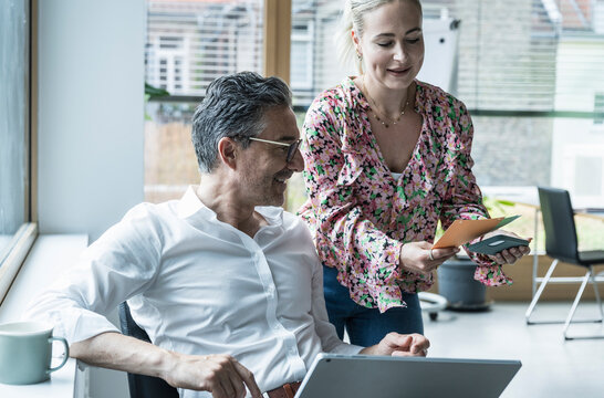Businesswoman showing envelope to businessman discussing in office