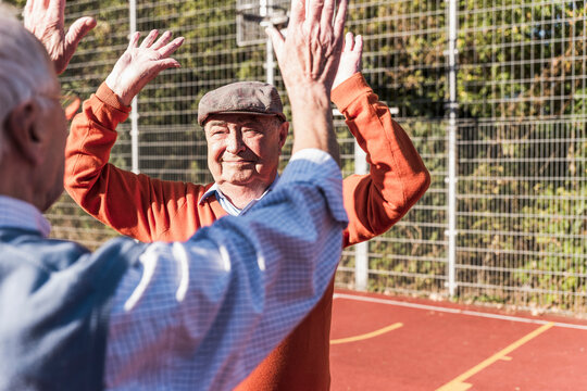 Active senior friends playing and giving high five at basketball court