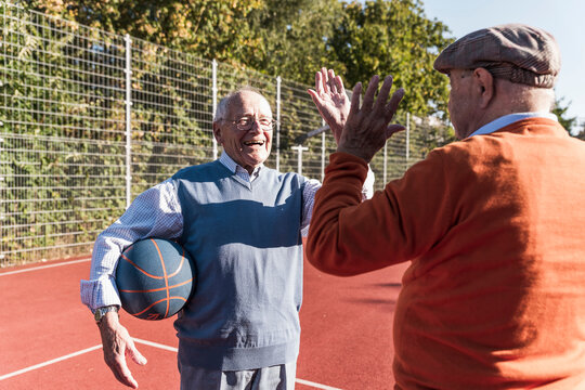 Happy friends playing and giving high five at basketball court