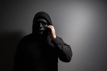 A man in a mask talking on the phone, gangster planning crime, masked thief evading security, dangerous person involved in illegal activity.