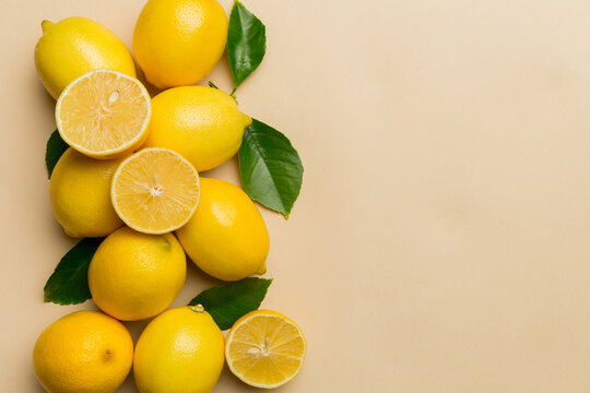 Many fresh ripe lemons with green leaves on colored background, top view, space for text