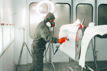 Auto mechanic worker wearing protective workwear spraying white paint on car part at workshop - Powered by Adobe