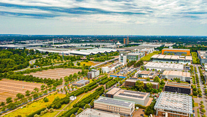 Aerial view of an extensive industrial and commercial area on the former Expo site in Hanover with large warehouses, office buildings and structured fields. Streets and paths divide the area.