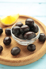 Black olives with lemon on wooden plate on blue background