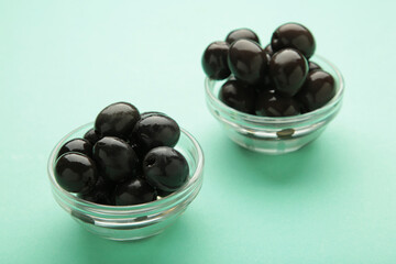 Black olives with lemon on bowl on mint background