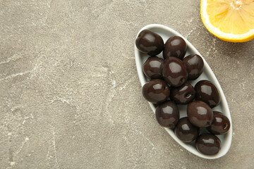 Fresh olives in white plate with lemon on grey concrete background.