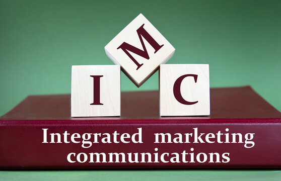 IMC - acronym on large wooden cubes on the background of a burgundy folder with the words INTEGRATED MARKETING COMMUNICATIONS