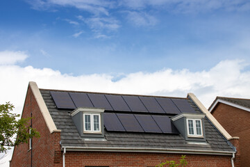 Photo of a modern British house in the UK with electrical solar panels on the roof on a bright sunny day with clouds in the sky