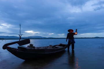 Obraz premium Asian fisherman on wooden boat casting a net for catching freshwater fish in nature river in the early morning before sunrise