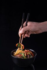 Hand using chopsticks pickup instant noodles with smokes isolated on black background.