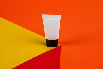 Plastic white tube for cream or lotion. Skin care or sunscreen cosmetic with stylish props on red and orange and yellow background.