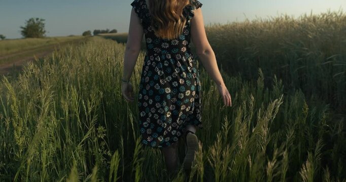 Young woman walking, enjoying the calm, peaceful and serene summer sunset with light shining on her hair during golden hour in cinematic slow motion.