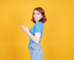 Obraz premium Side view portrait of young caucasian red bob hair 20s woman using mobile phone looking camera wear wireless earphones smiling satisfied. Using application, typing message chatting online.