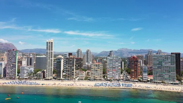 Aerial drone footage of the beautiful city of Benidorm in Spain in the summer time showing the Playa de Levante beach and high rise apartments and hotels on the beach front on a sunny day