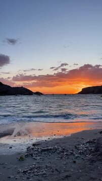 Vertical video. Beautiful sunset at the beach. Ibiza beach. Summer vacation. Beach with waves of blue calm water, ocean coast with tranquil relaxing waves, vacations concept.