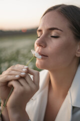 A woman is sitting in a field and smelling a flower. Concept of peace and tranquility, as the woman is enjoying the simple pleasure of smelling a flower.