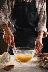 Close-up of female hands beating eggs in a transparent bowl using a whisk. Dark background.